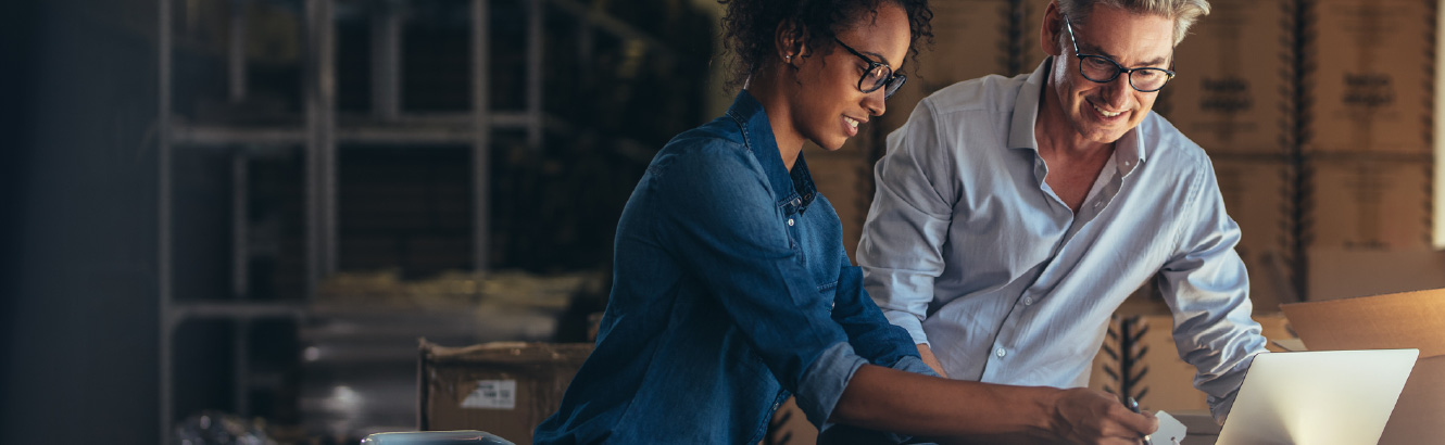 Two workers filling a box with items. One is holding a laptop.