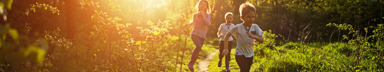 Three school-aged children running through a green field.