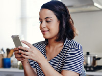 A woman in a kitchen looking at a smartphone.