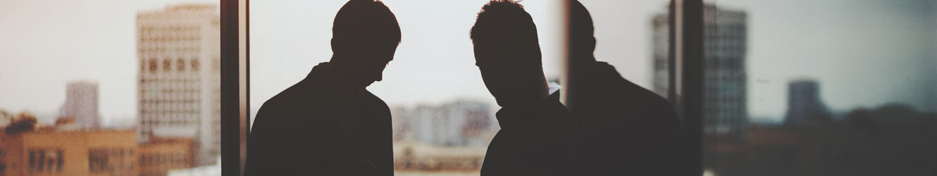 Two businessmen silhouettes against a large window.