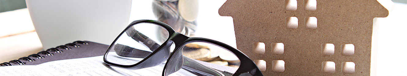 Close up of various items on a desk, including a pair of black glasses.