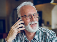 A man with grey hair and glasses talking on the phone.