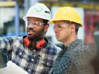 Two workers in hardhats standing together and looking at something in the distance.